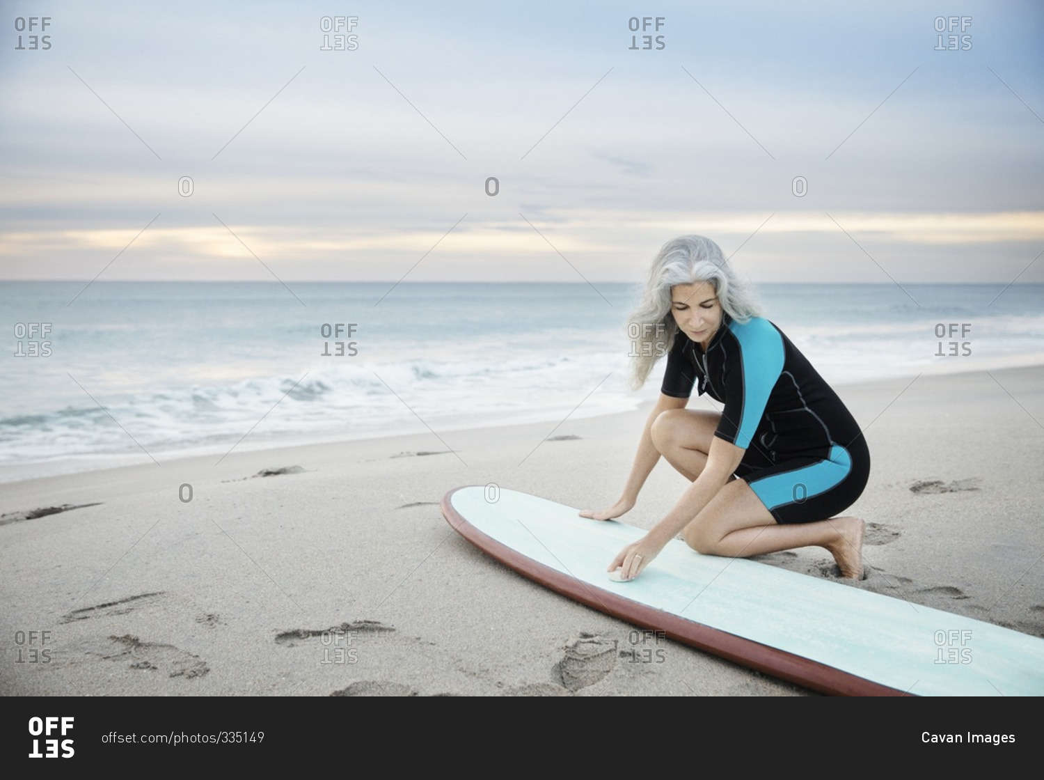 Woman Kneeling On The Beach And Waxing Her Surfboard Stock Photo Offset