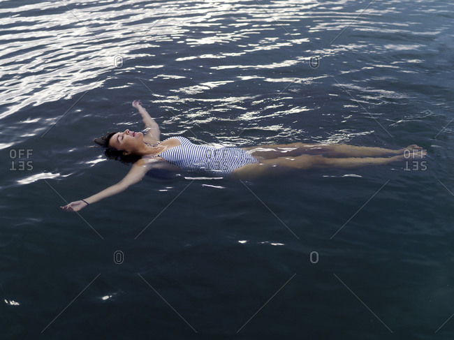 High angle view of woman floating on back in water arms outstretched looking up