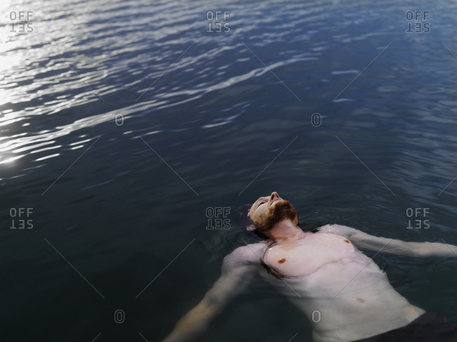 High angle view of young man floating on back in water arms outstretched looking up