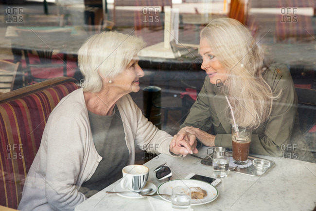 Mother and daughter sitting together in cafe, holding hands, seen through cafe window