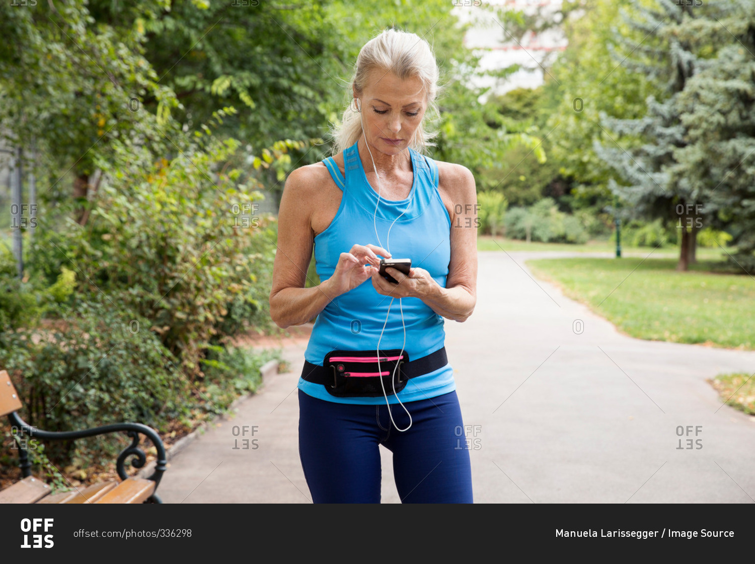 Mature woman choosing smartphone music whilst training in park