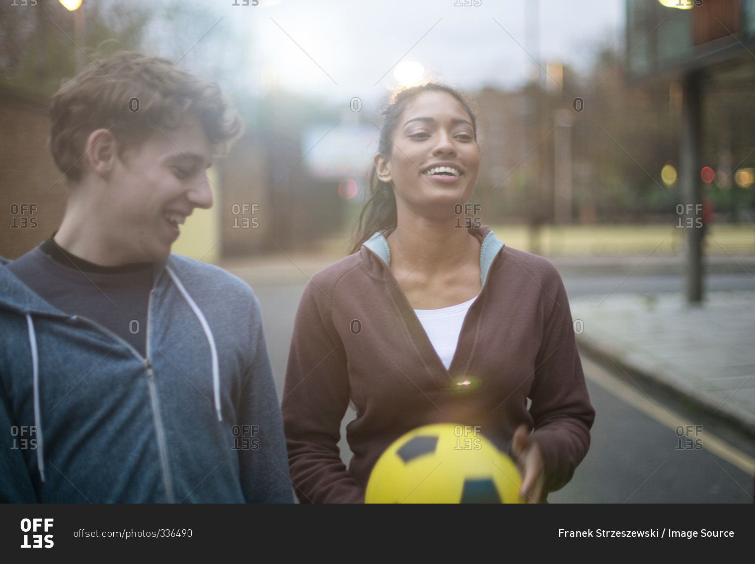 Young man and woman walking in street, holding soccer