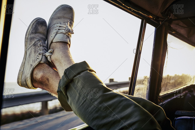Man rests in back seat of car with dirty shoes hanging out window