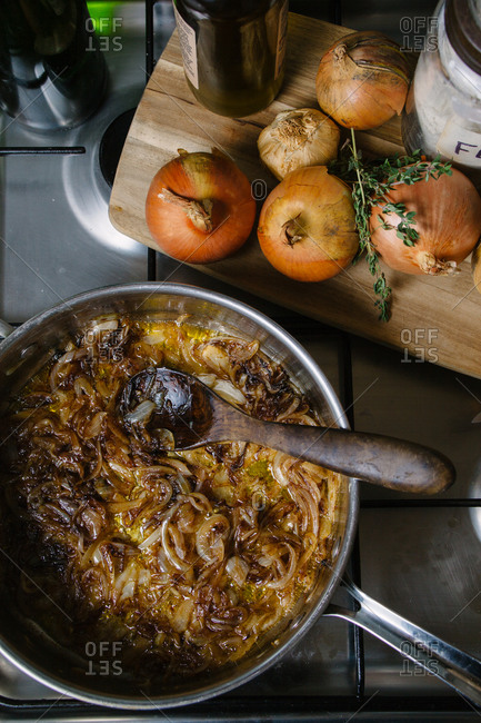 Caramelized onions in a pan on a stove with whole onions