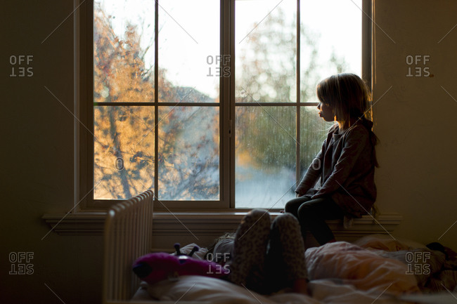 Girl staring out window by bed stock photo - OFFSET