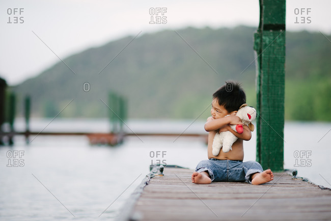 Little boy sitting on a dock hugging his stuffed animal