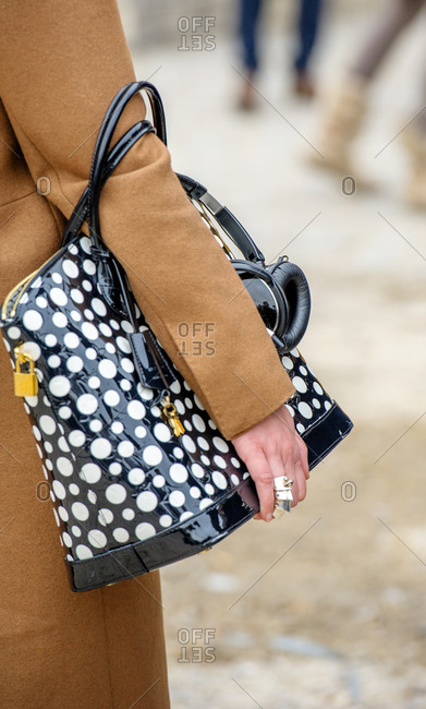 Model wearing camel coat and polka dots leather bag with headphones