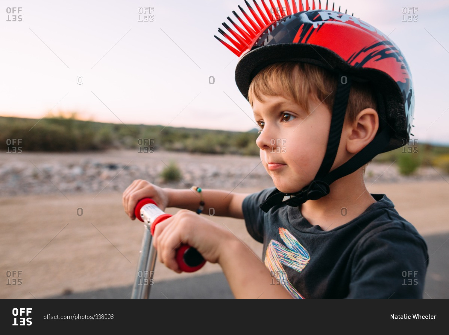 Little boy in a spiked helmet holding scooter handlebars stock