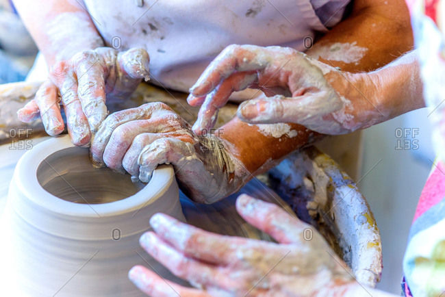 Close up of female potter and mature student hands making pot on potters wheel