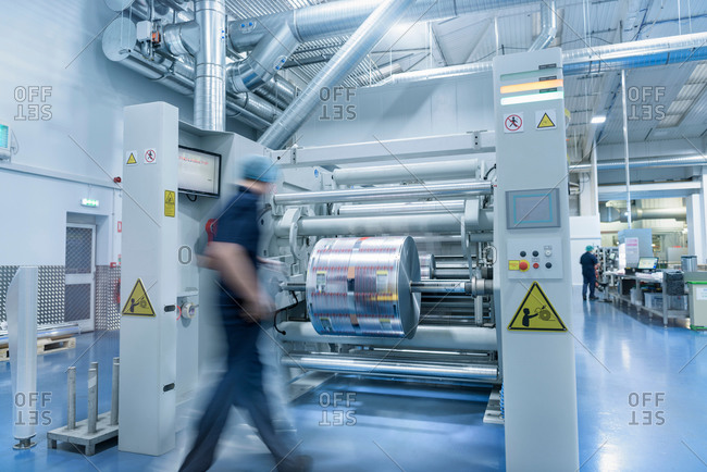 Worker walking by printed roll in food packaging printing factory