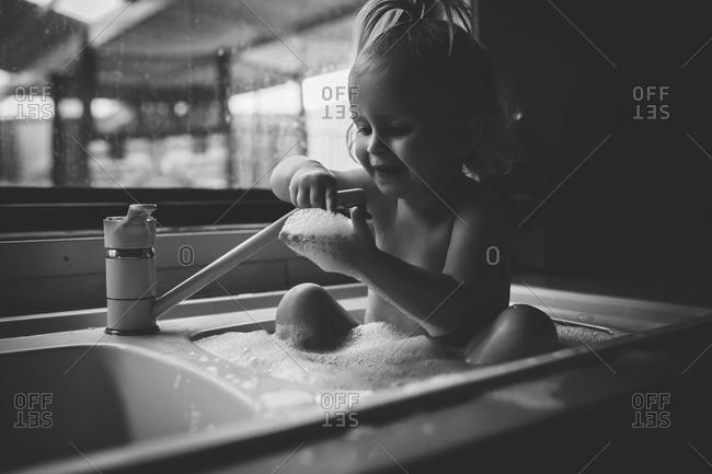 Little girl taking a soapy bath in the kitchen sink