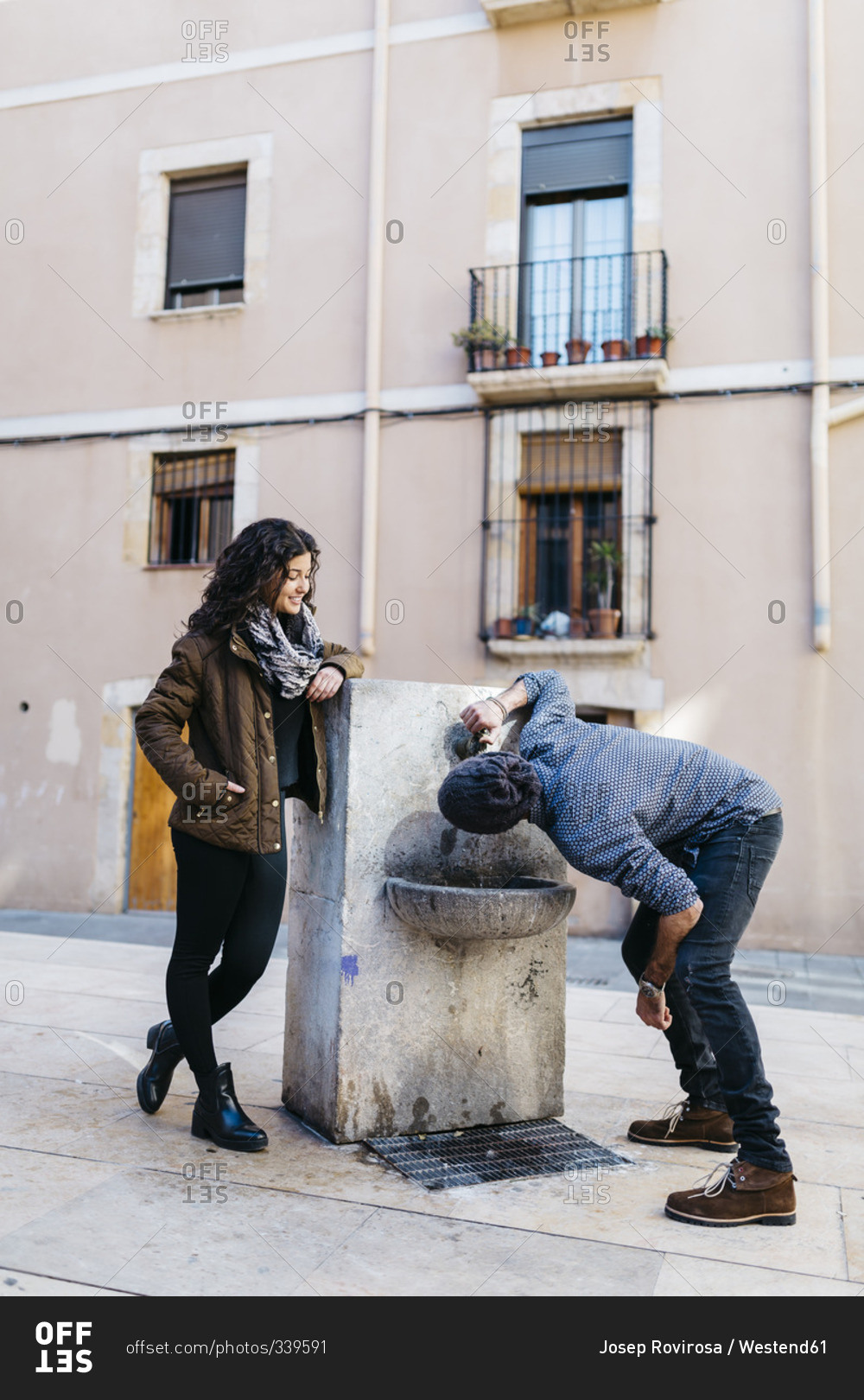 Spain, Tarragona, Young couple, man drinking from drinking fountain