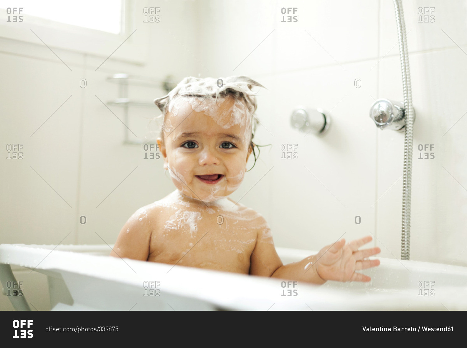Portrait of smiling baby boy with foam in his hair sitting in bathtub