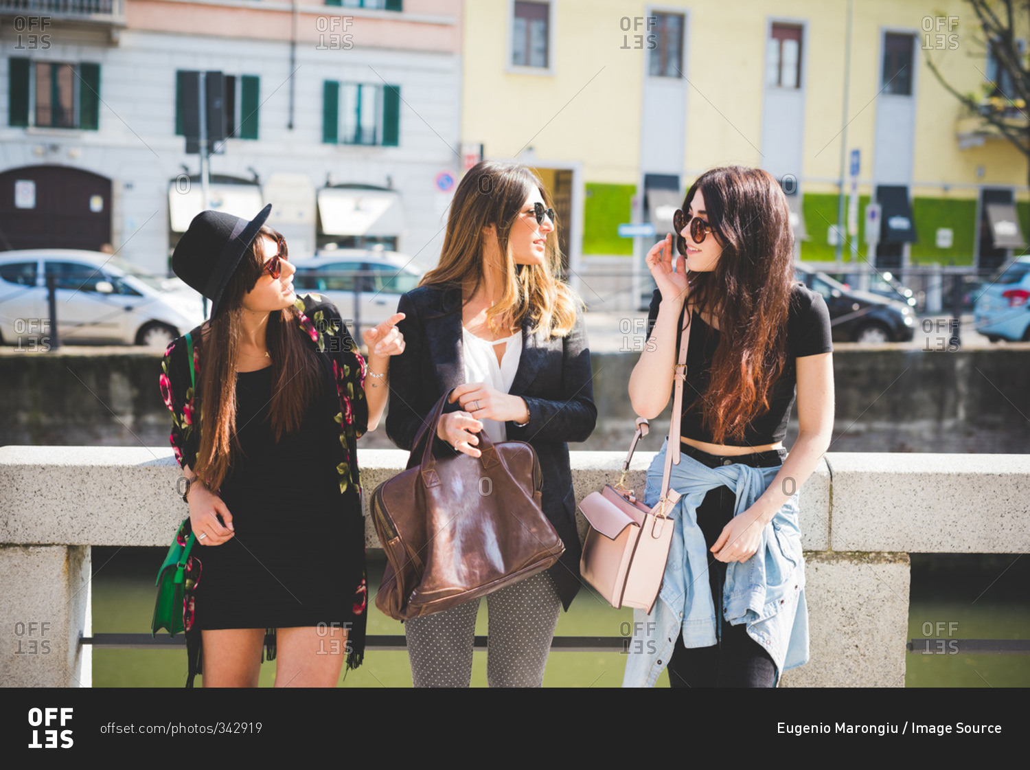 Three stylish young female friends chatting at city riverside