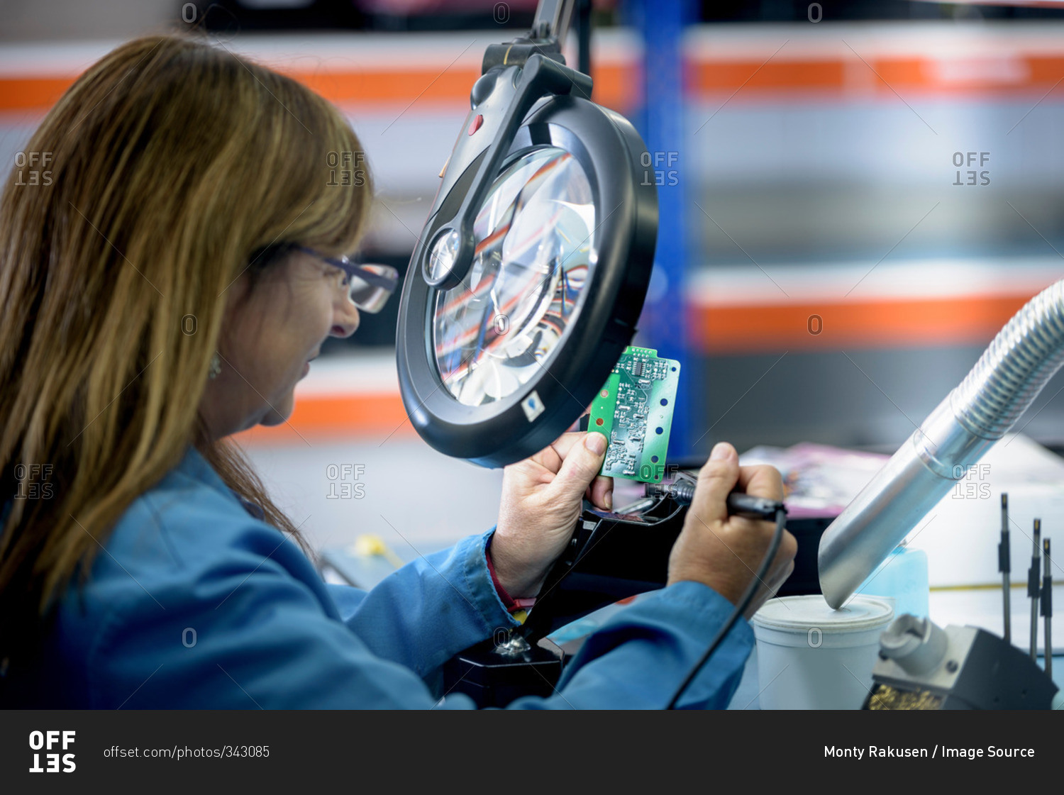 Female worker soldering electronic parts in clean room in electronics factory