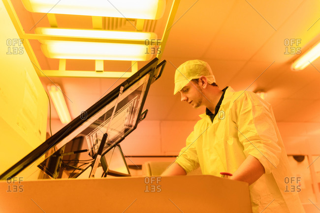 Worker printing circuit board under photographically safe light in circuit board factory