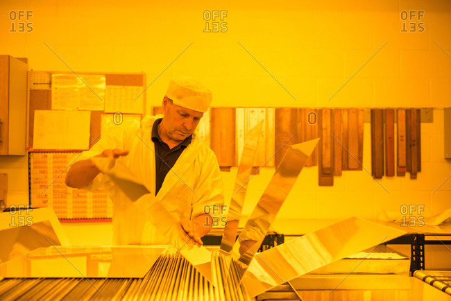 Worker inspecting circuit board under photographically safe light in circuit board factory