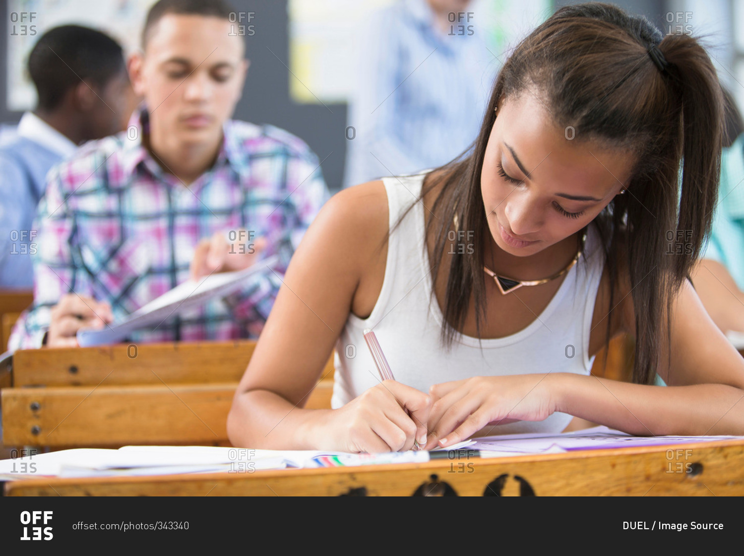 Female student, sitting at desk in classroom, writing
