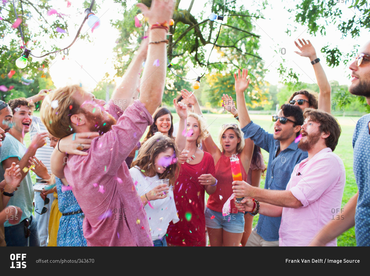 Adult crowd celebrating with arms raised at sunset party in park