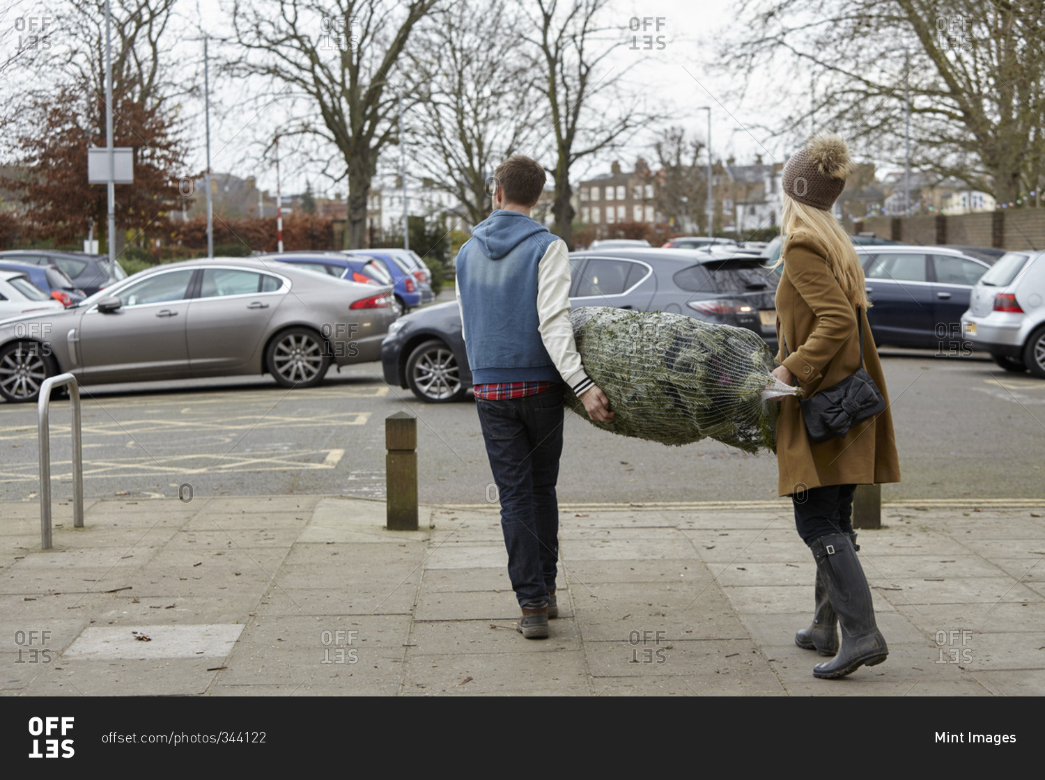 Two people carrying a netted Christmas tree to the car park