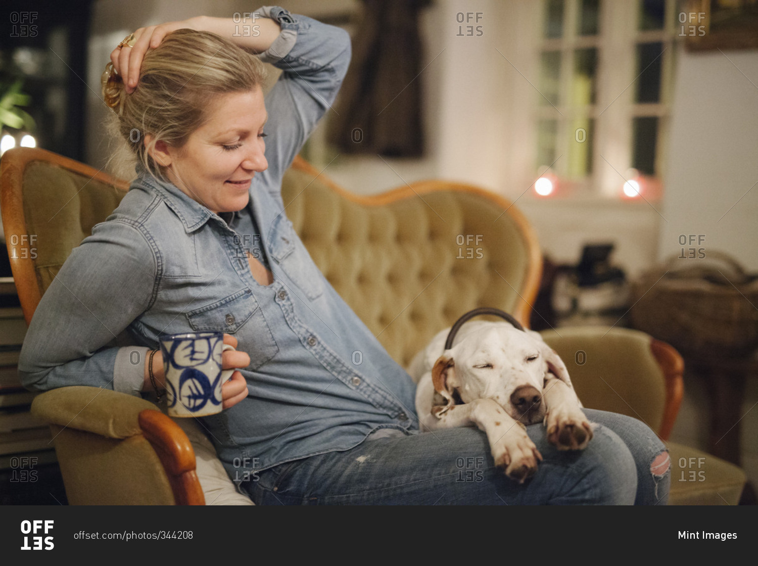 A woman seated on a sofa with a dog with his head on her lap