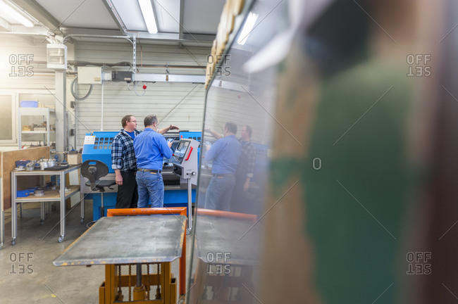 Two men in factory talking at 	eroding machine