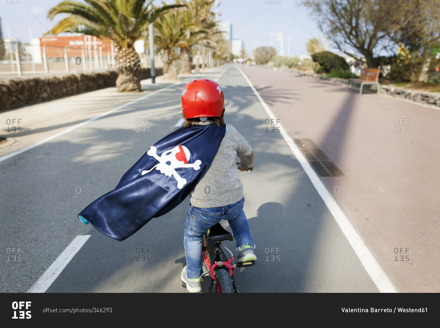 Spain, Barcelona, back view of little boy with a pirate cape riding bicycle on an empty street