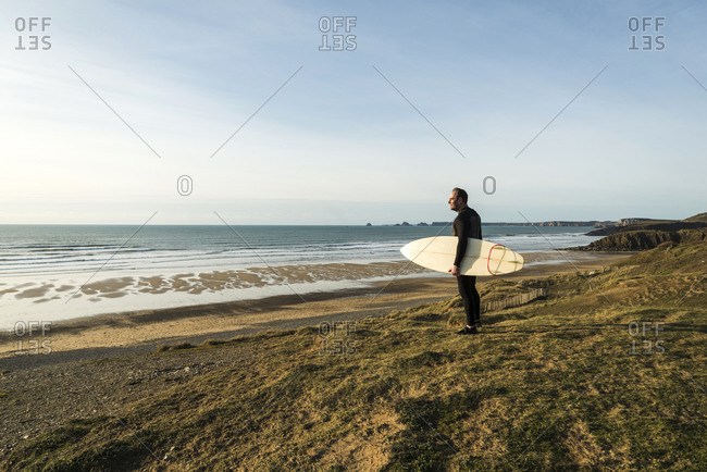 France, Bretagne, Finistere, Crozon peninsula, man standing at the coast with surfboard