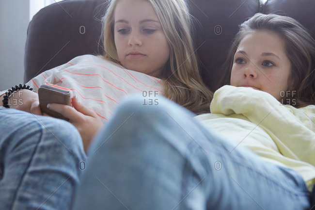 Two girls watching TV and smartphone texting on sofa