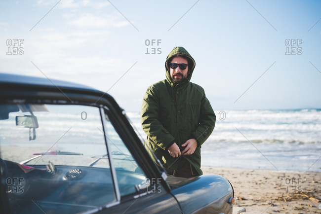 Mid adult man with vintage car fastening anorak on beach, Sorso, Sassari, Sardinia, Italy