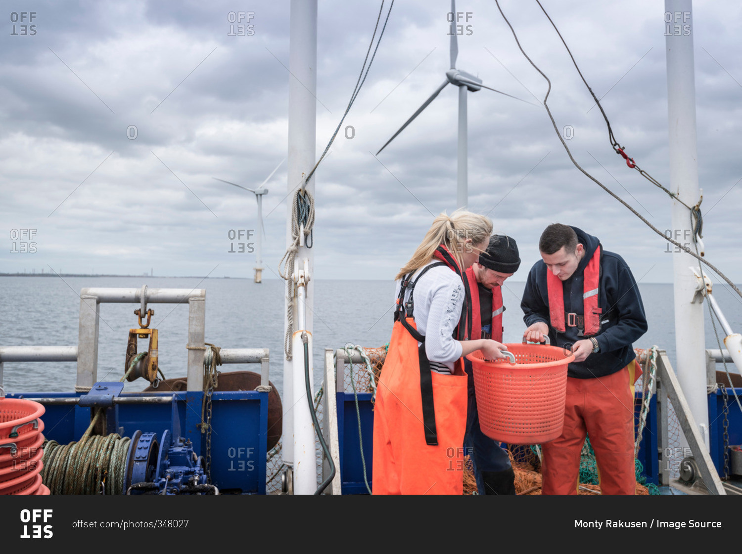 Research scientists and fisherman inspecting catch of fish on deck of research ship