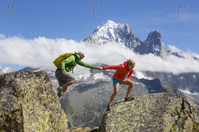 A female hiker is helping a male hiker to jump over a wide gap between two rocks in the mountains of Chamonix, France.
