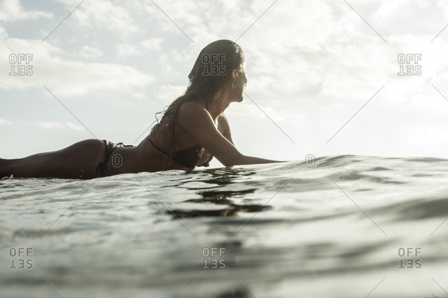 Latin American girl waits for a wave on her surf board while surfing at sunset