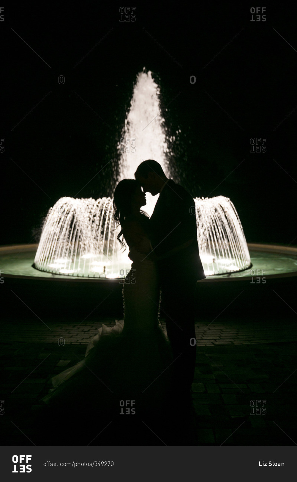 Silhouette of bride and groom in front of a fountain at night