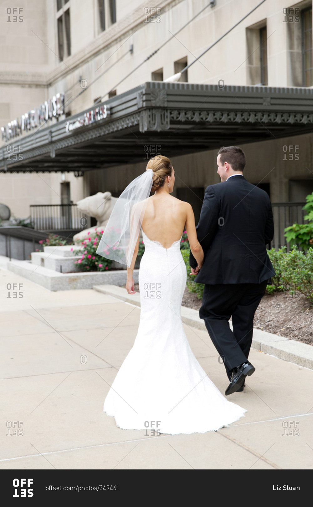 Newlyweds holding hands and walking toward the entrance of an elegant building