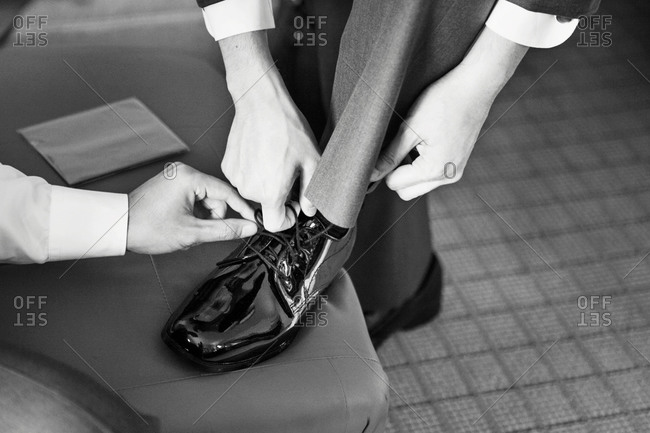 Groom tying his shoe before a wedding with help from a groomsman