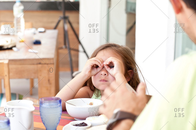 Father and daughter sitting at breakfast table, daughter making binoculars from fingers