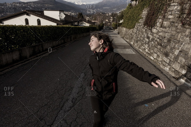 Girl walking up a narrow road with her eyes closed and head turned away