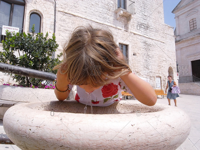 Puglia, Italy - August 15, 2010: Girl drinking from a water fountain in Puglia, Italy