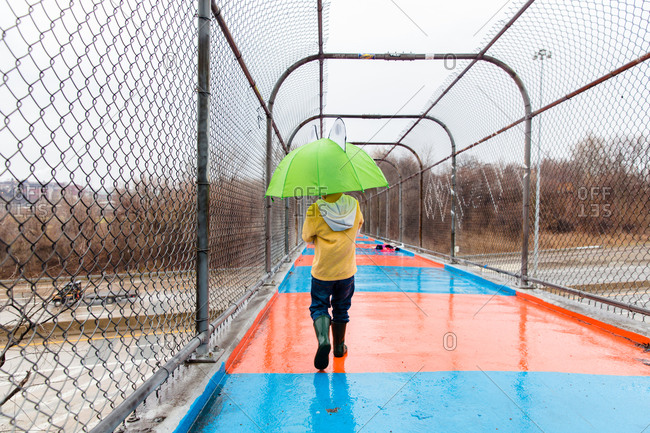 Young child with a frog umbrella and rain boots on pedestrian bridge