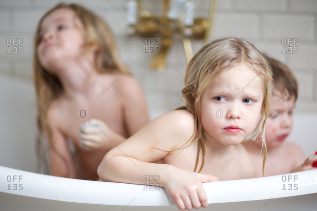 Little girl in bathtub with siblings looking with curiosity