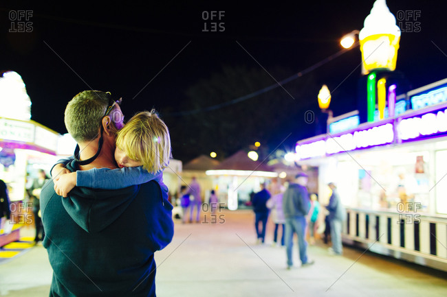 Man carrying his son through a fairground at the end of the day