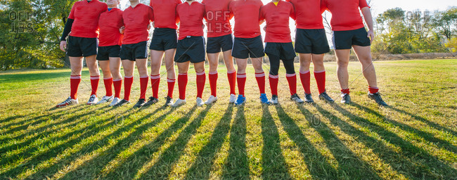 Rugby players together in line preparing to make a huddle with focus on legs and shadows