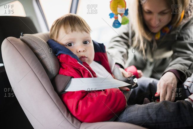 Woman fastening seat belt of his little son sitting in child's seat in a car