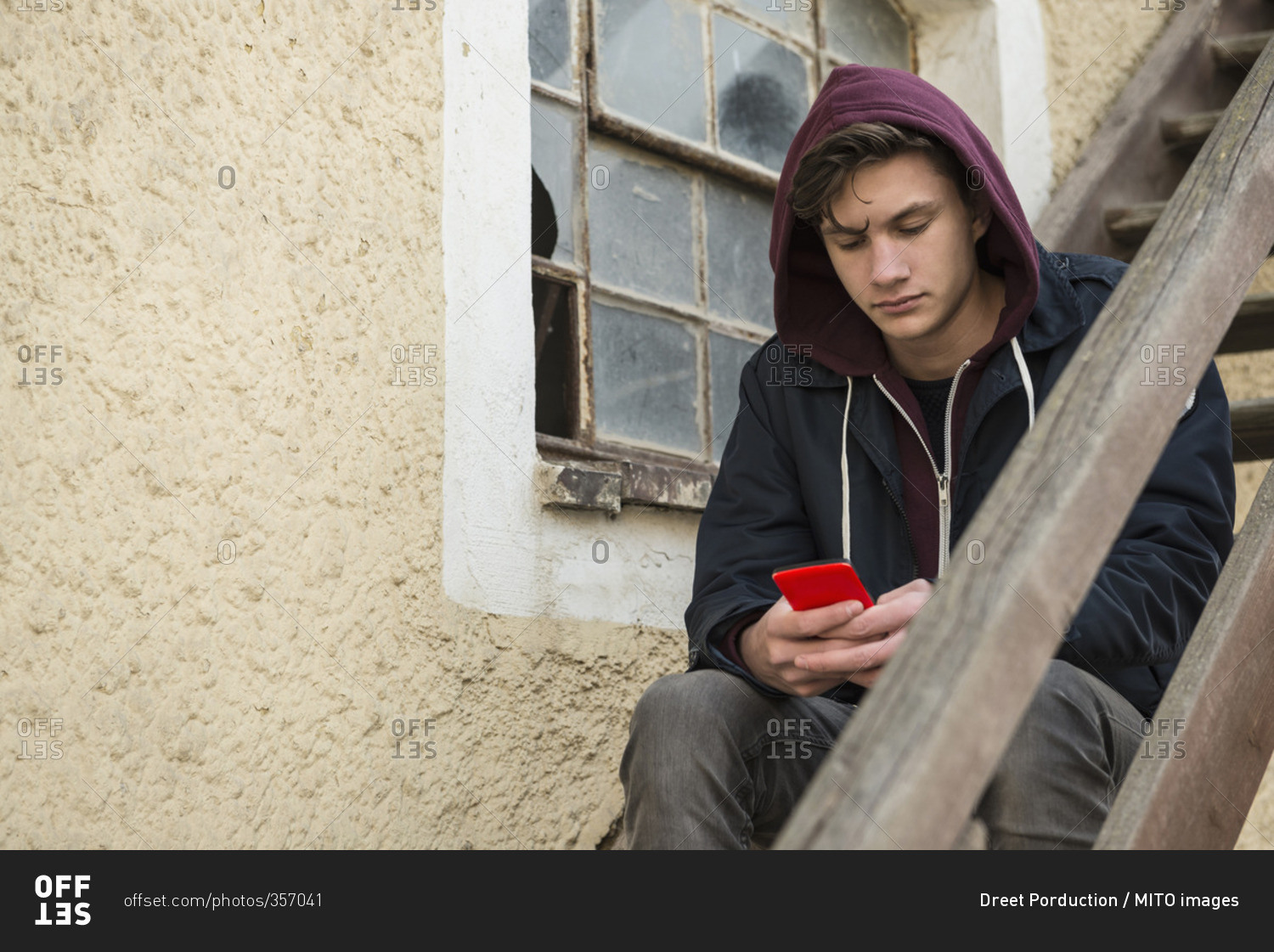 Young man text messaging on phone and sitting on wooden stairs, Munich, Bavaria, Germany