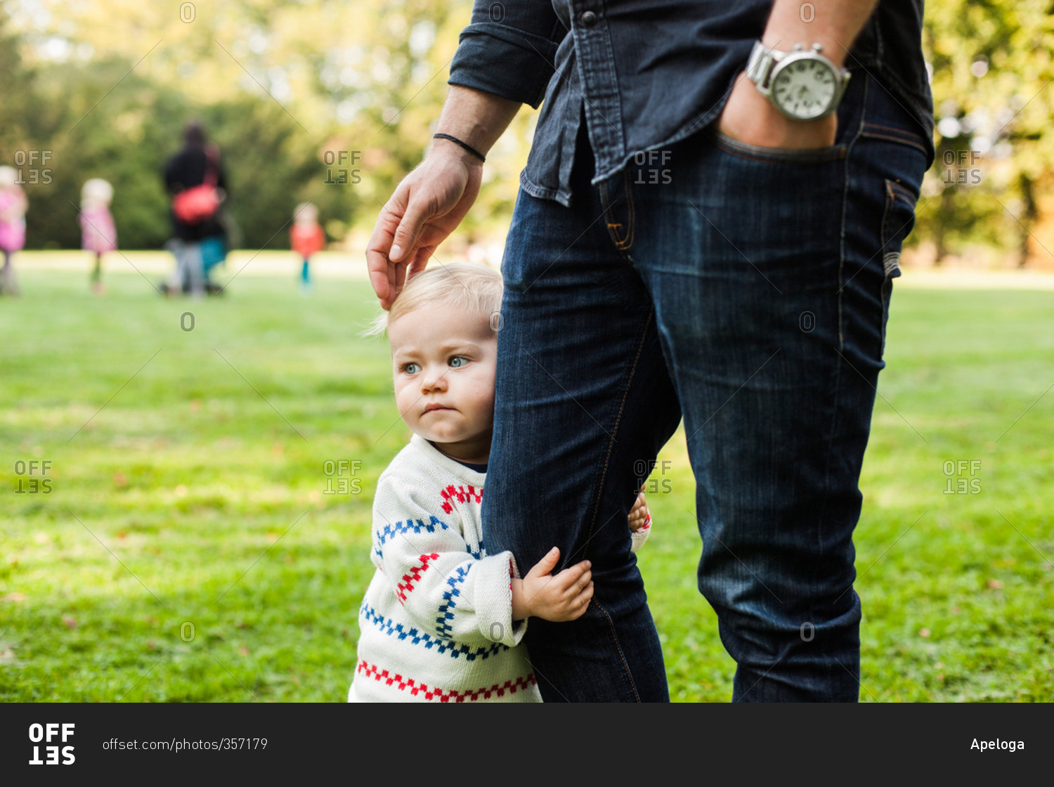 Baby girl holding father's leg in park