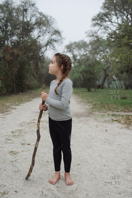 Young girl standing barefoot on dirt road with a stick