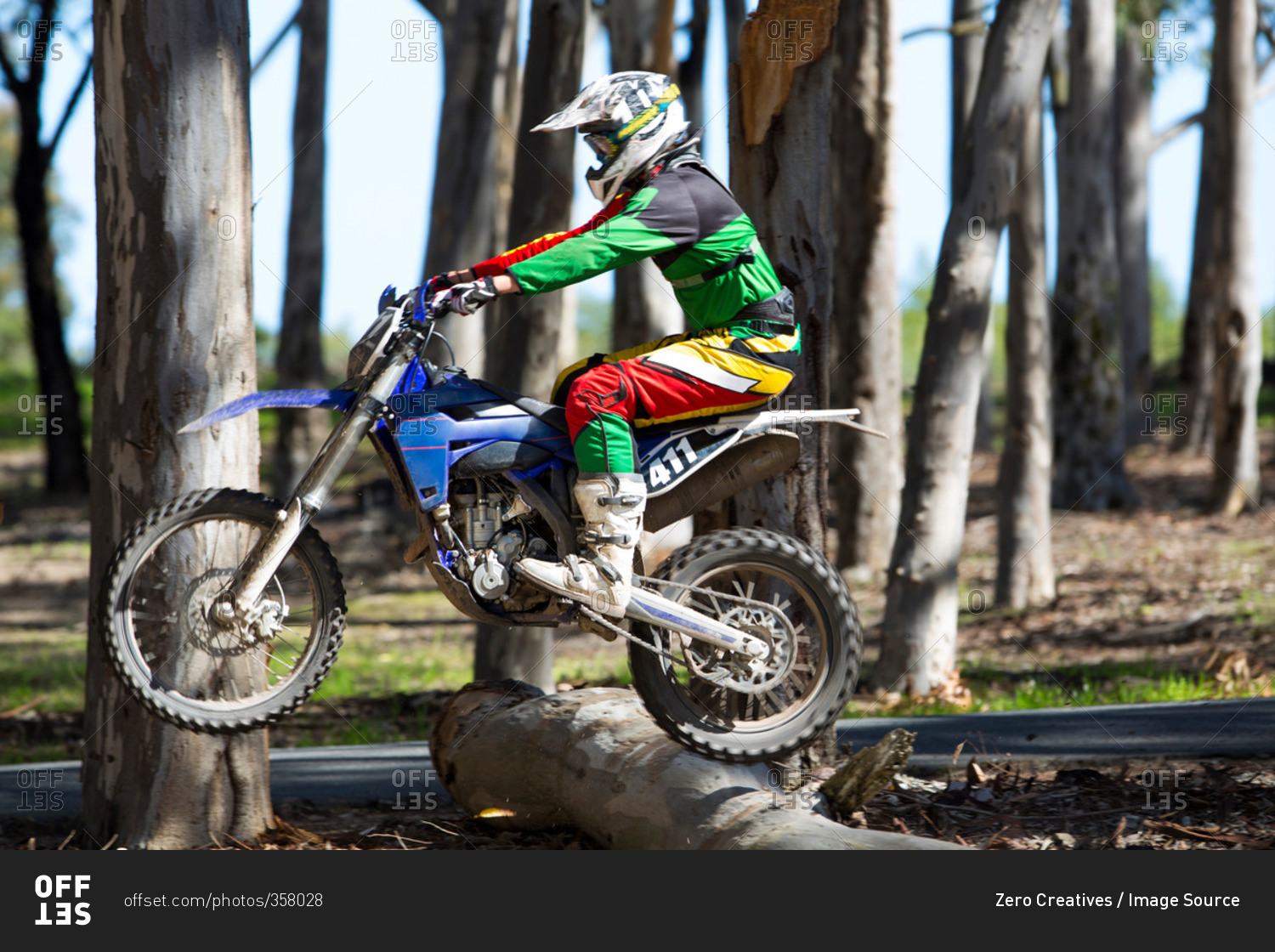 Young male motocross racer jumping on top of forest logs
