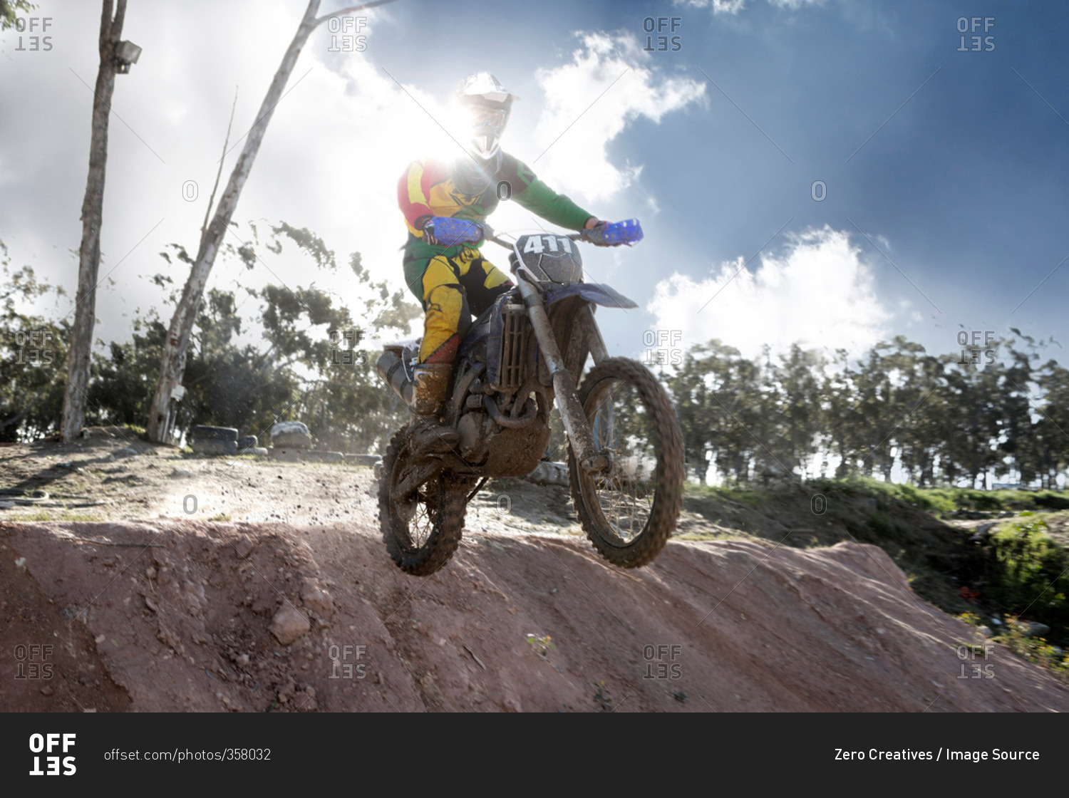 Young male motocross racer jumping mid air down mud hill