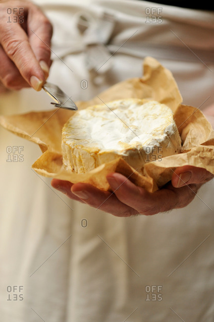 Man holding goats cheese and cheese knife, focus on hands